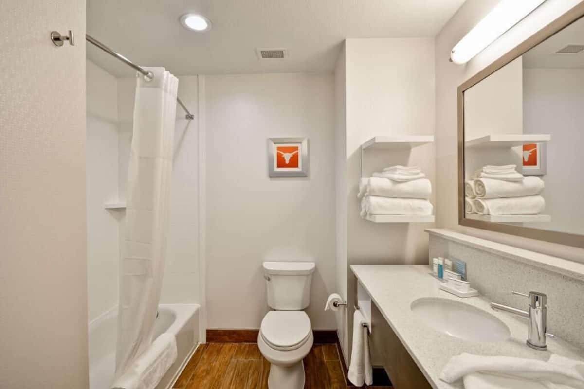A bathroom with a shower, toilet, sink, and towel racks.