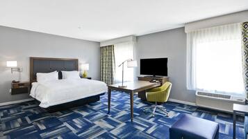 A hotel room with a large bed, a desk with a chair, a television, and an air conditioning unit.