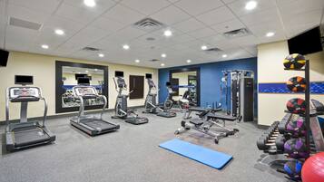 Un gimnasio equipado con cintas de correr, elípticas, bancos de pesas y varias pelotas de ejercicio.