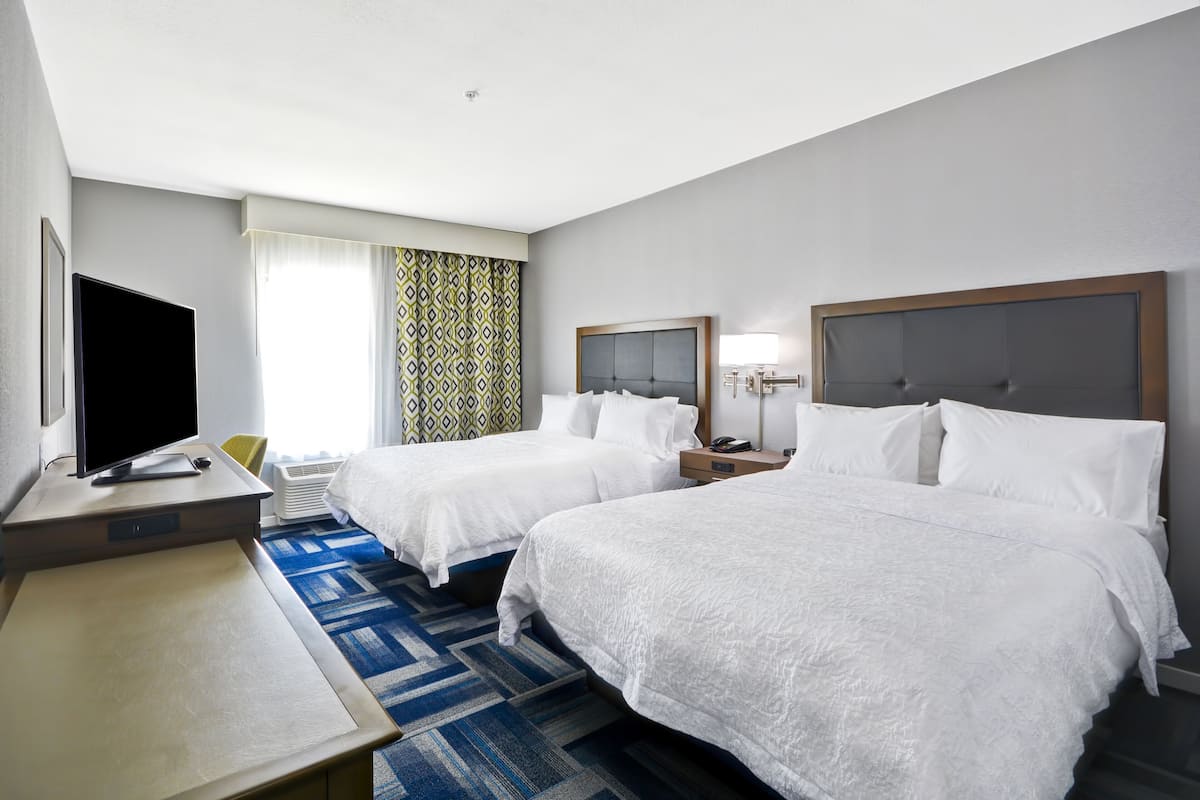 A hotel room with two beds, a desk with a TV, and a patterned curtain.