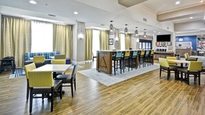 A hotel dining area with a long table, multiple chairs, and a bar area. - Hampton Inn Kyle (Kyle)