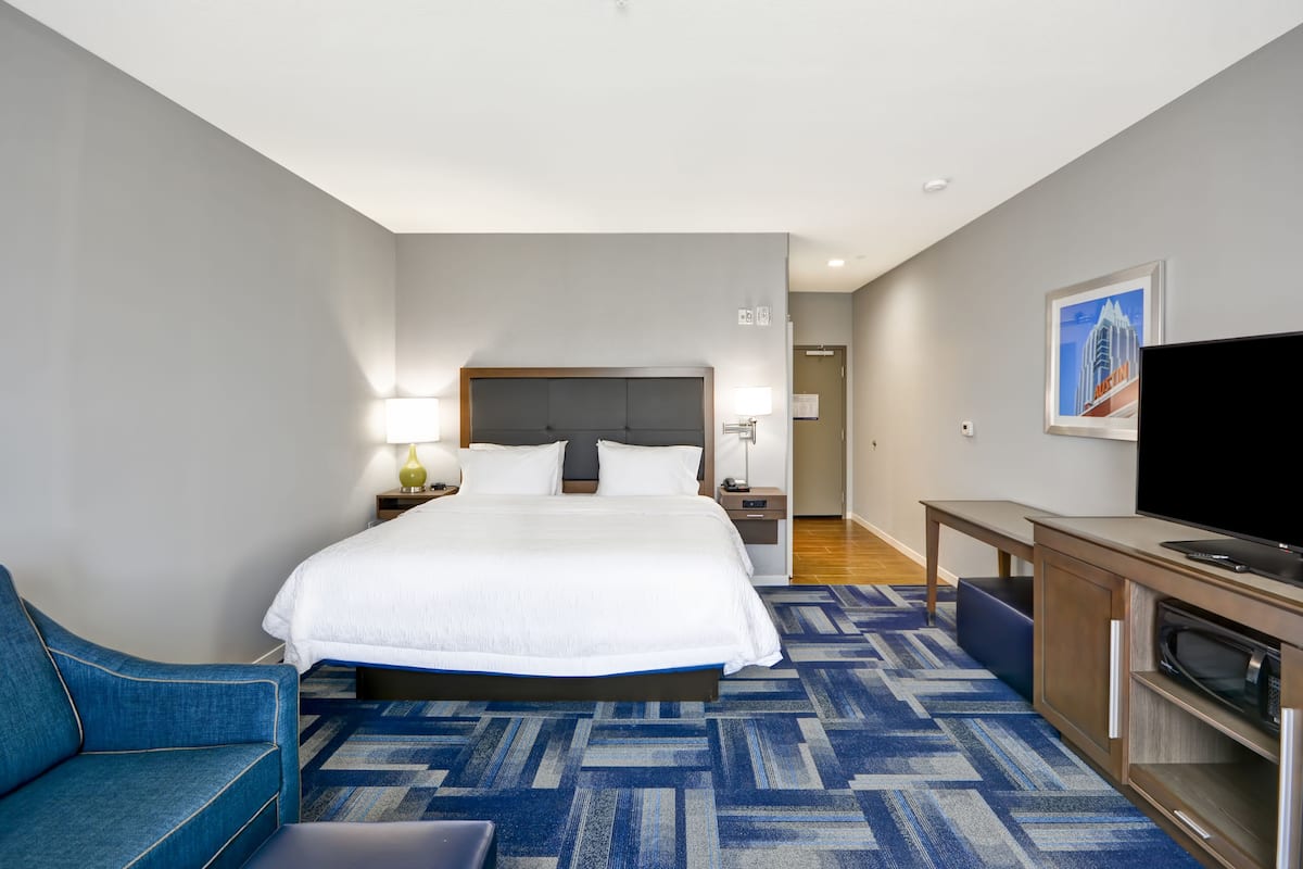 A hotel room with a large bed, a TV, a desk, and a blue armchair.