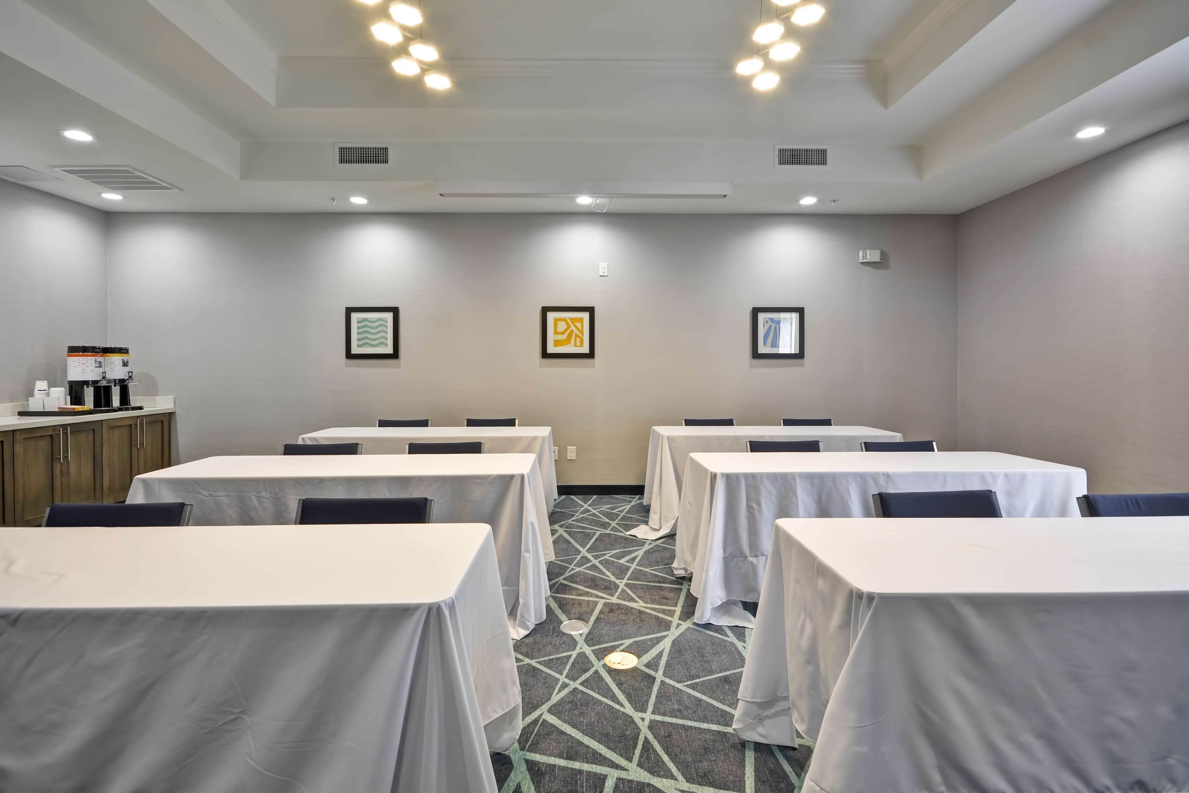 Un salón de conferencias con mesas cubiertas de manteles blancos, una alfombra estampada y obras de arte enmarcadas en las paredes.