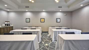 Uma sala de conferências com mesas cobertas por toalhas brancas, um tapete estampado e quadros decorativos nas paredes.