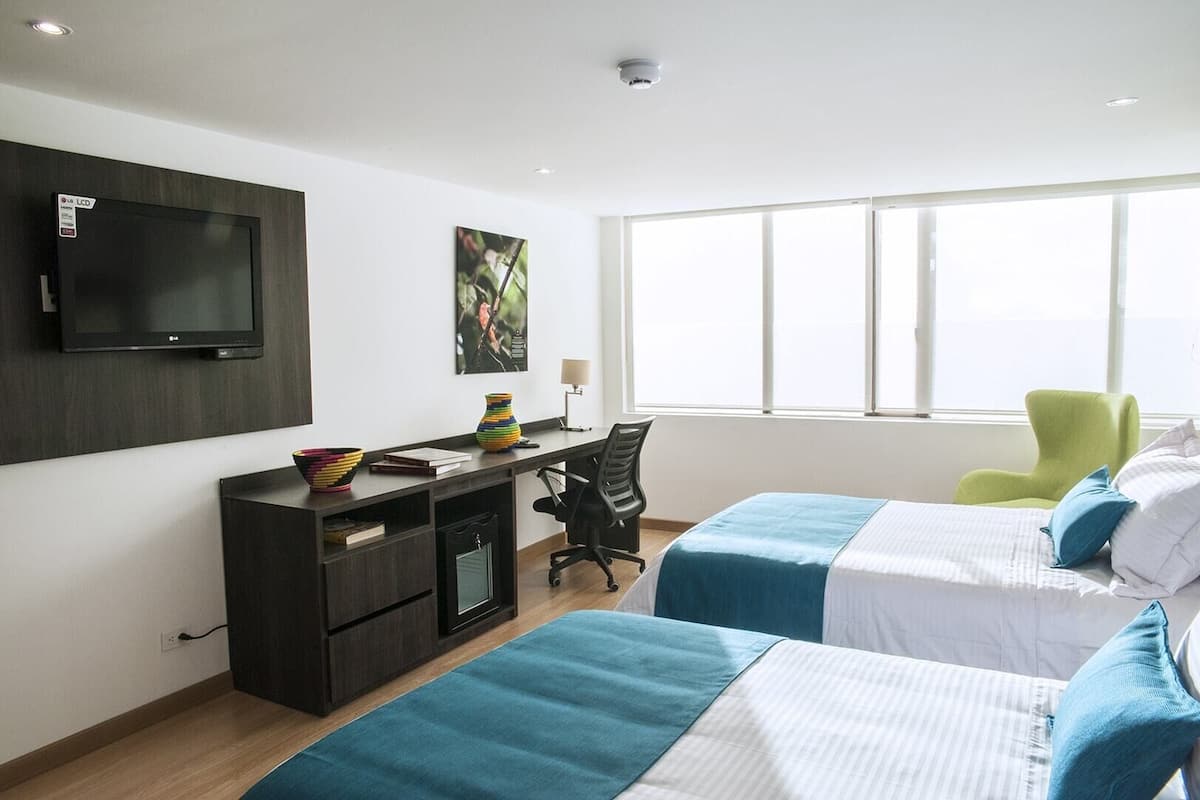 A hotel room with a desk, two beds, a TV, and a window with a view.