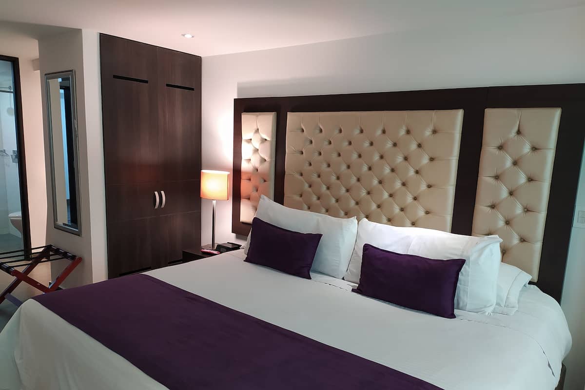 A hotel room with a large bed, a wooden wardrobe, a nightstand with a lamp, and a mirror.