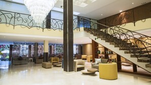 A spacious lobby with a grand chandelier, a modern staircase, and comfortable seating areas.