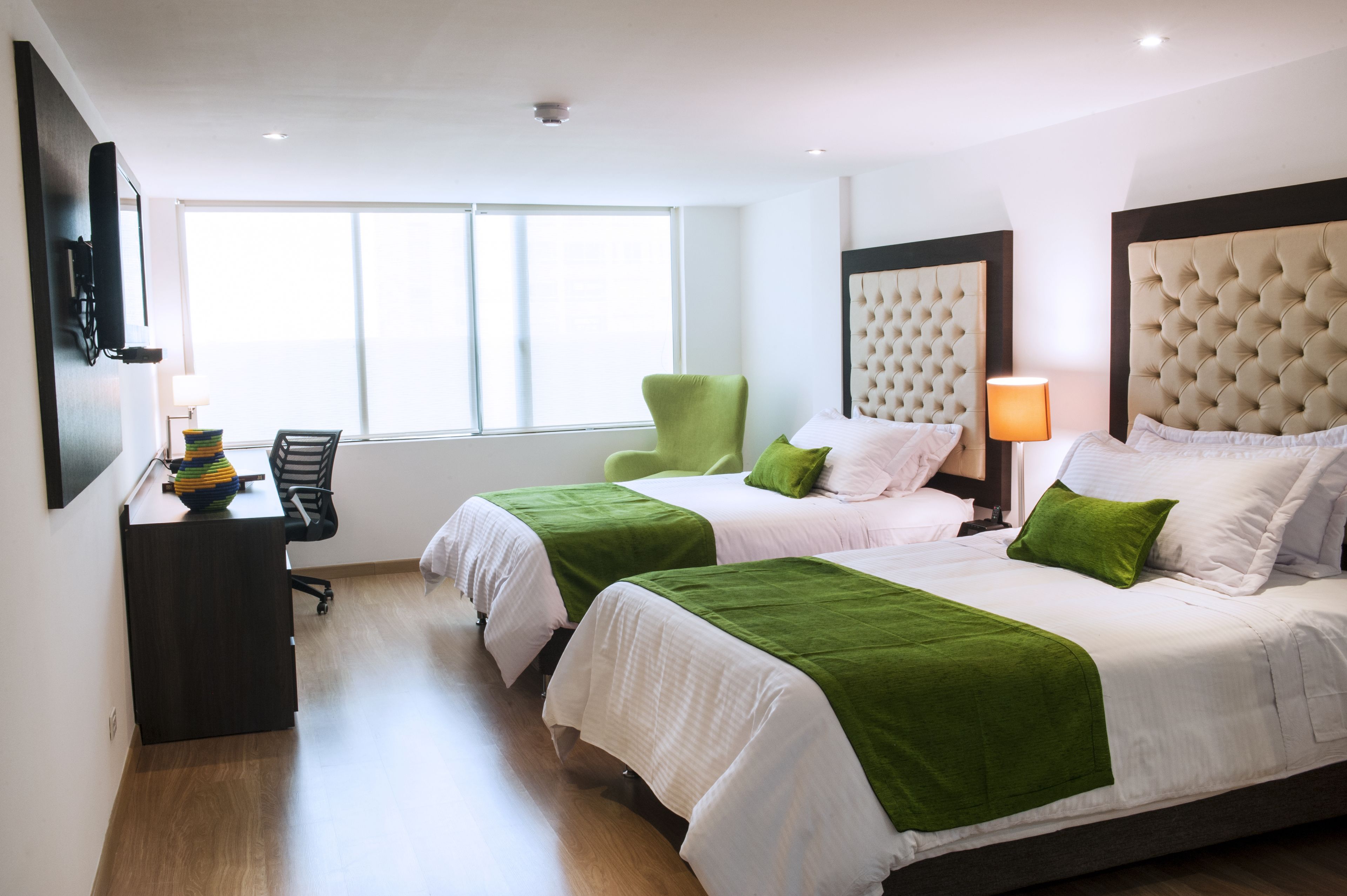 A hotel room with two beds, a desk, a chair, and a large window.