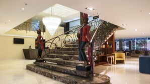 A modern hotel lobby with a marble staircase, a chandelier, and a seating area with a sofa and armchairs.