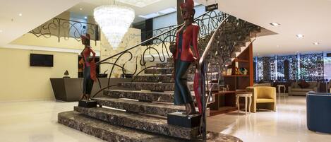 Eine moderne Hotelhalle mit einer Marmortreppe, einem Chandelier und einer Sitzecke mit einer Couch und Sesseln.