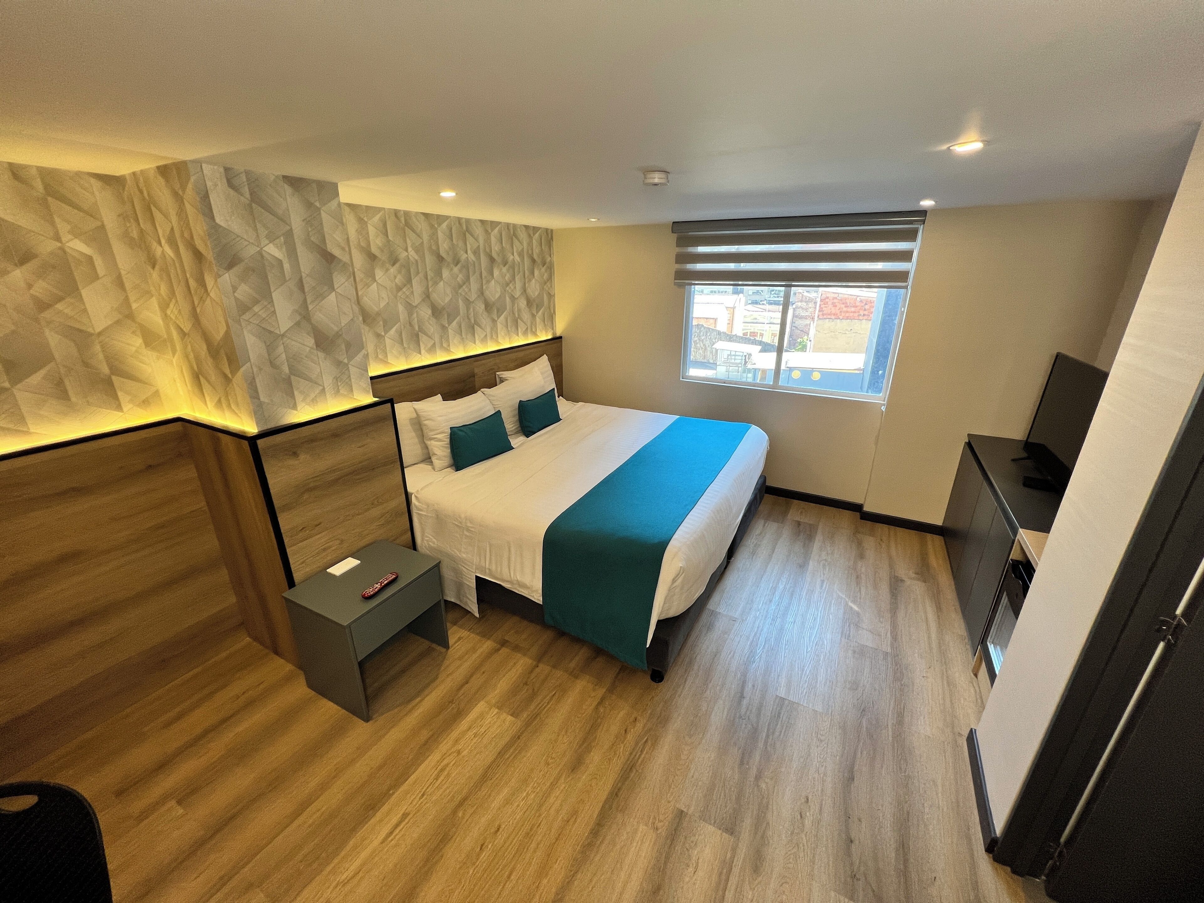 Una camera d'albergo moderna con un letto grande, un comodino, una TV e una finestra con vista sull'esterno.