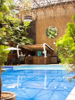 Una piscina interior con una terraza de madera, rodeada de abundante vegetación y un muro rústico.