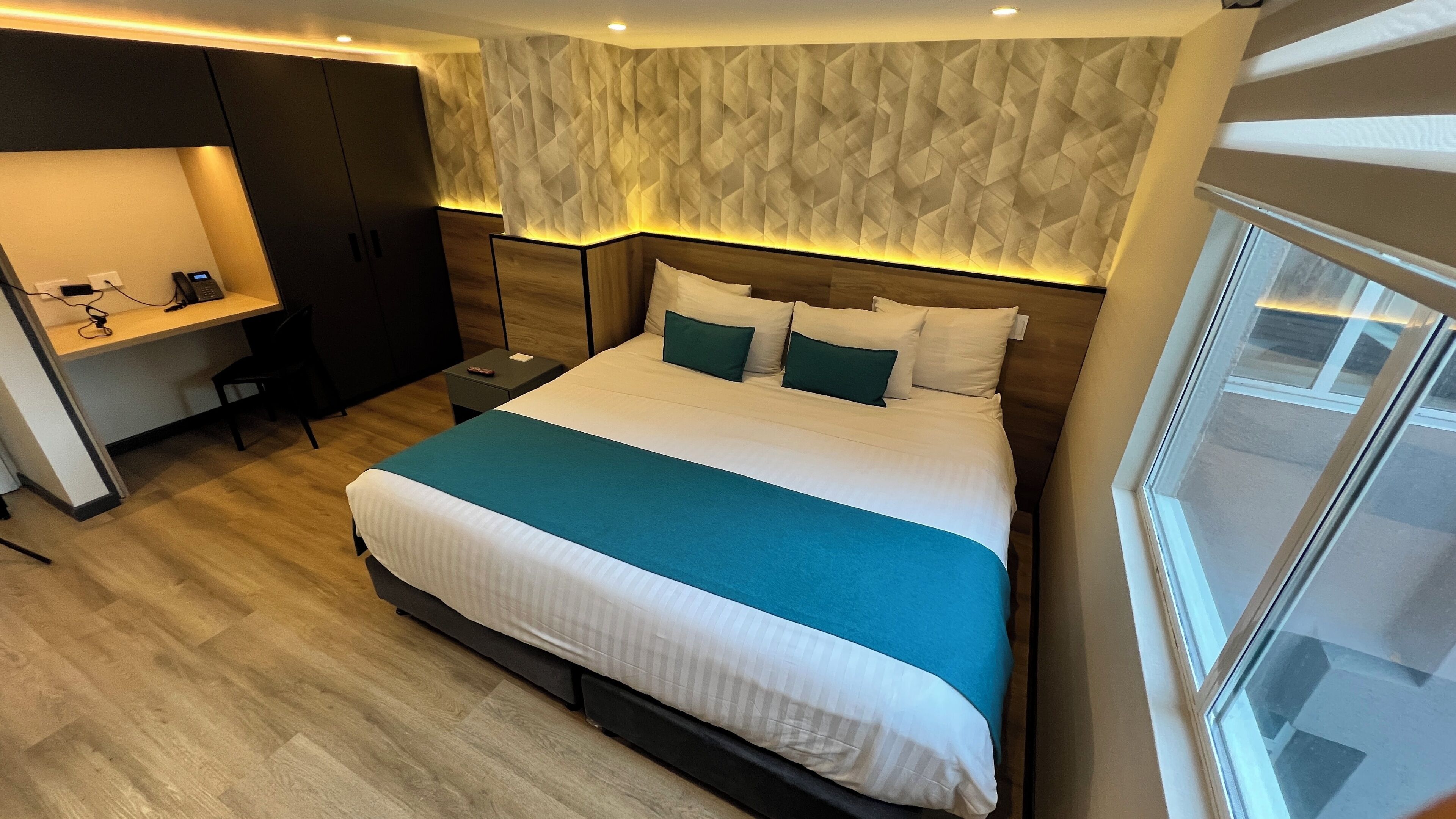 A modern hotel room with a large bed, a desk, and a wardrobe.
