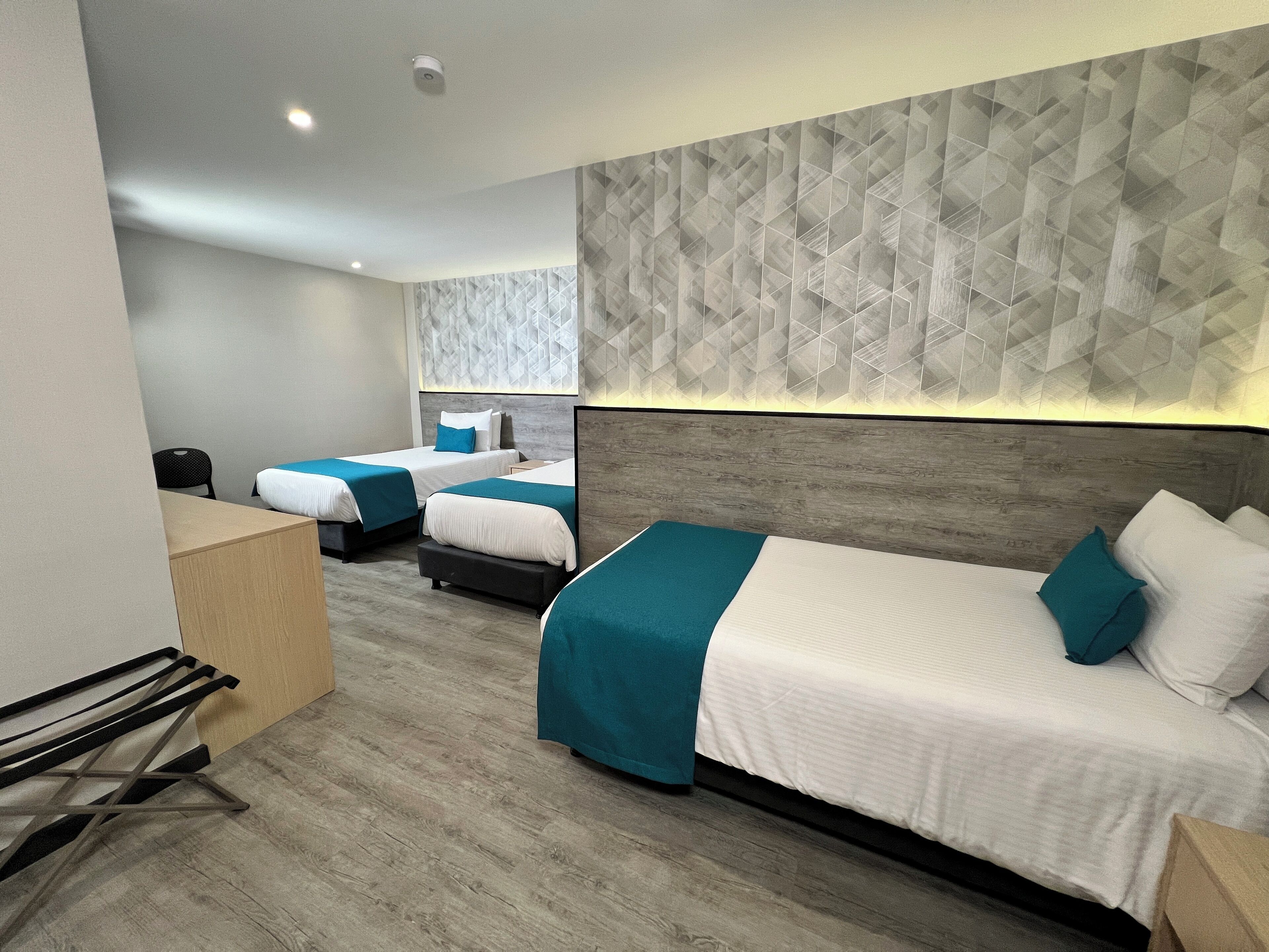 Habitación de hotel con tres camas, suelo de madera y pared con estampado geométrico.