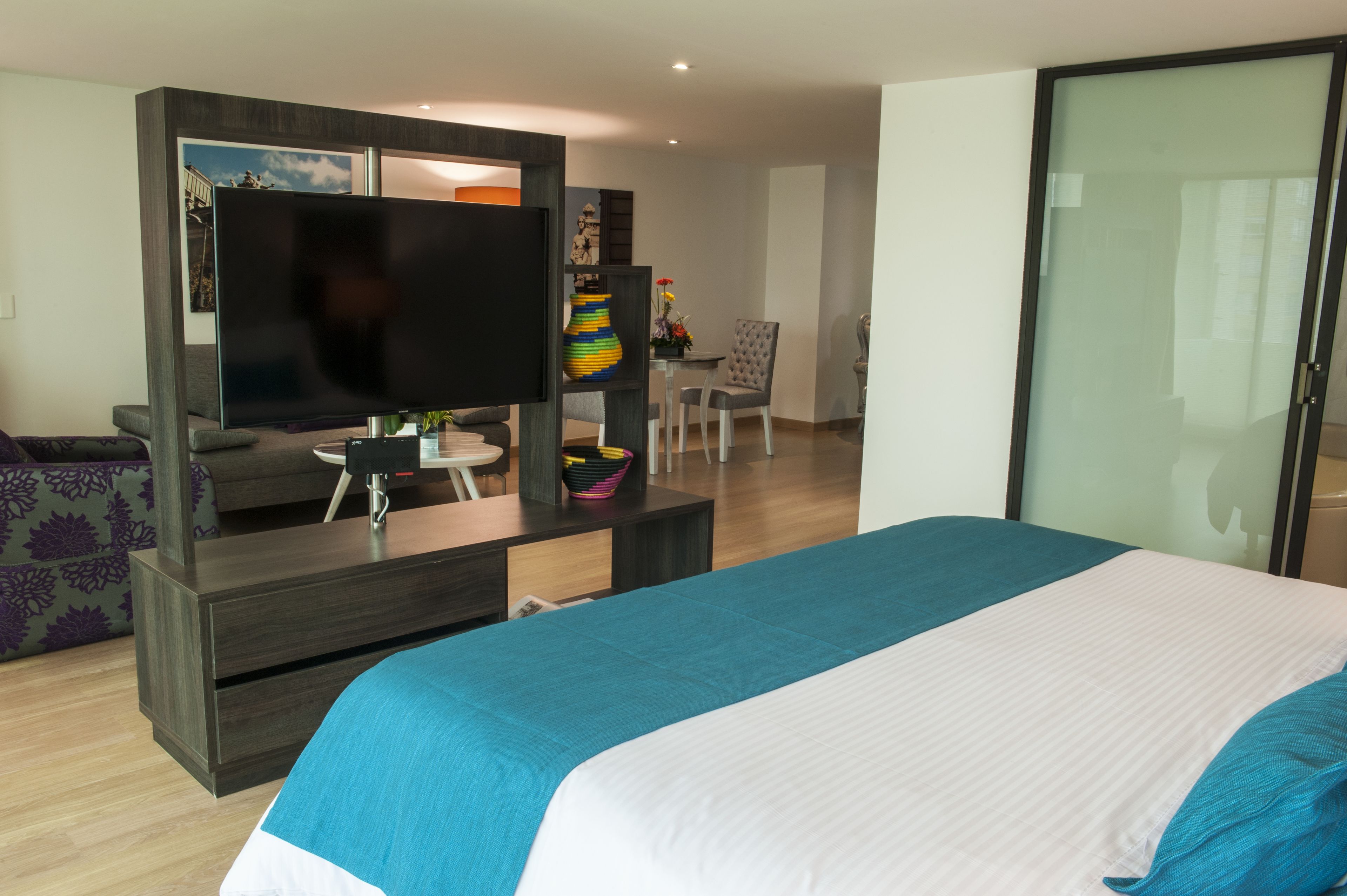 Una habitación de hotel moderna con una cama grande, un televisor de pantalla plana, un escritorio con una silla y una zona de comedor con mesa y sillas.