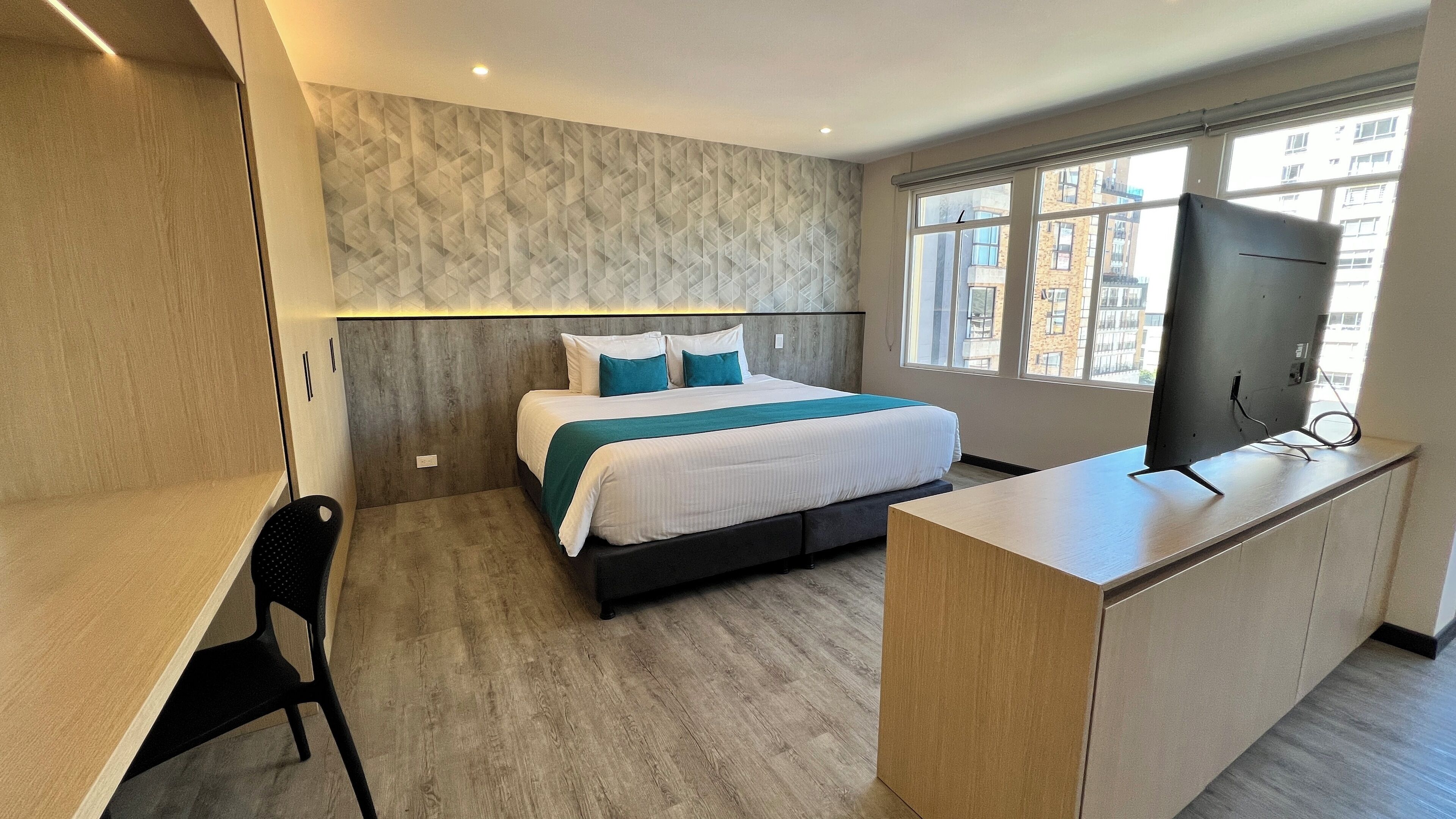 Une chambre d’hôtel moderne équipée d’un lit, d’un bureau, d’une télévision et d’une fenêtre donnant sur la ville.