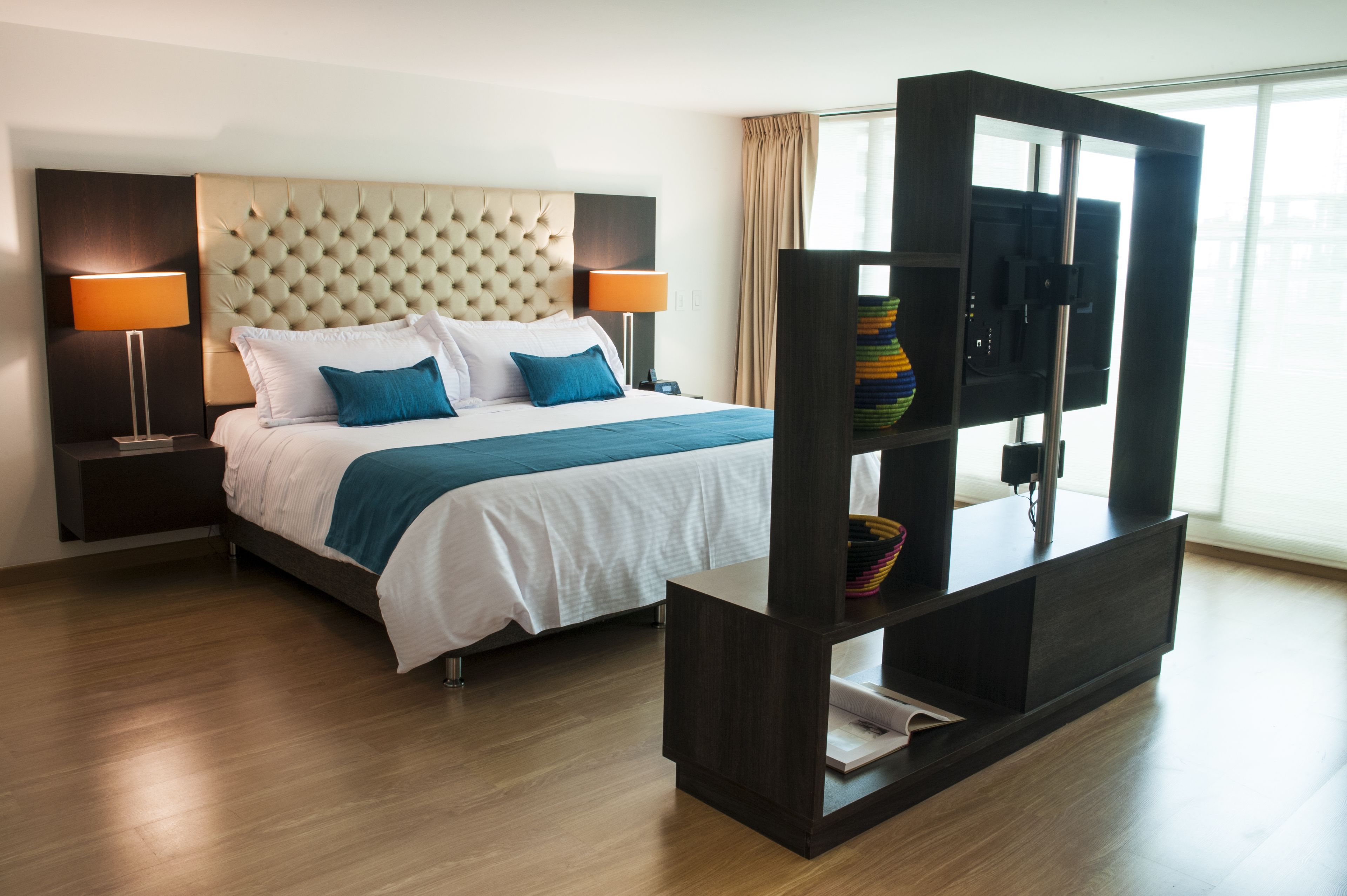 Une chambre d’hôtel moderne avec un grand lit, deux lampes de chevet, un téléviseur à écran plat posé sur un meuble en bois et une grande fenêtre avec des rideaux.