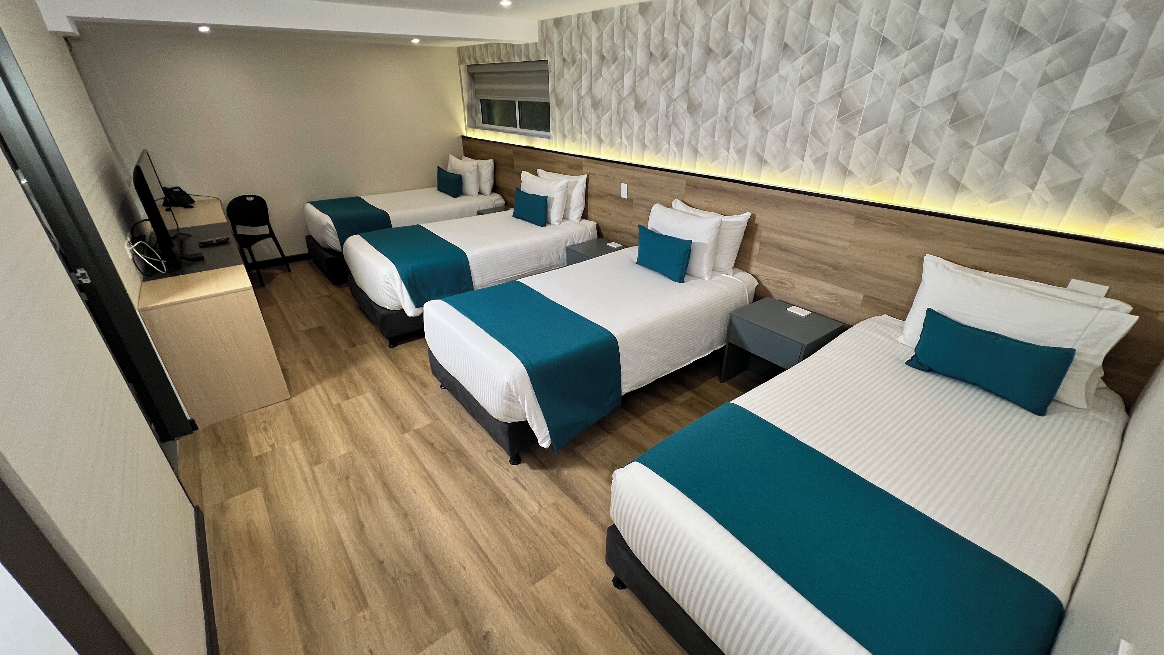 A hotel room with four single beds, a desk, a chair, and a television.