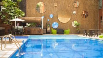 Una piscina con cubierta de madera, zona de estar y bar.