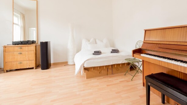 A bedroom with a wooden bed, a piano, a dresser, and a mirror. - Peters Wohnung (Weimar)