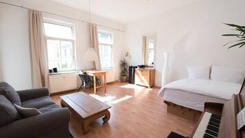 Relax in a serene space with a large bed, sofa, and desk, surrounded by natural light and lush greenery.