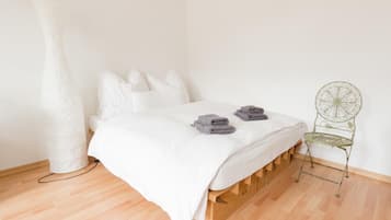 Ein schlicht eingerichtetes Schlafzimmer mit einem hölzernen Bettgestell, weißer Bettwäsche und einem grünen Metallstuhl.