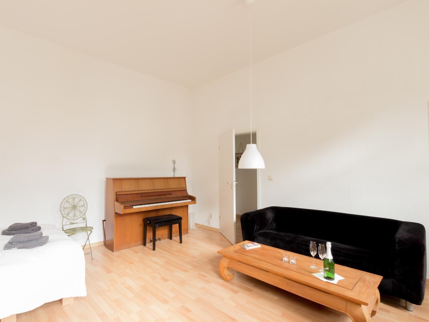 Un salon moderne avec un piano, un canapé noir, une table basse en bois et un luminaire suspendu.