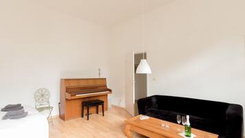 Un salon moderne avec un piano, un canapé noir, une table basse en bois et un luminaire suspendu.