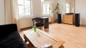A modern living room with a wooden coffee table, a black sofa, a dining table, and a large window. - Peters Wohnung (Weimar)
