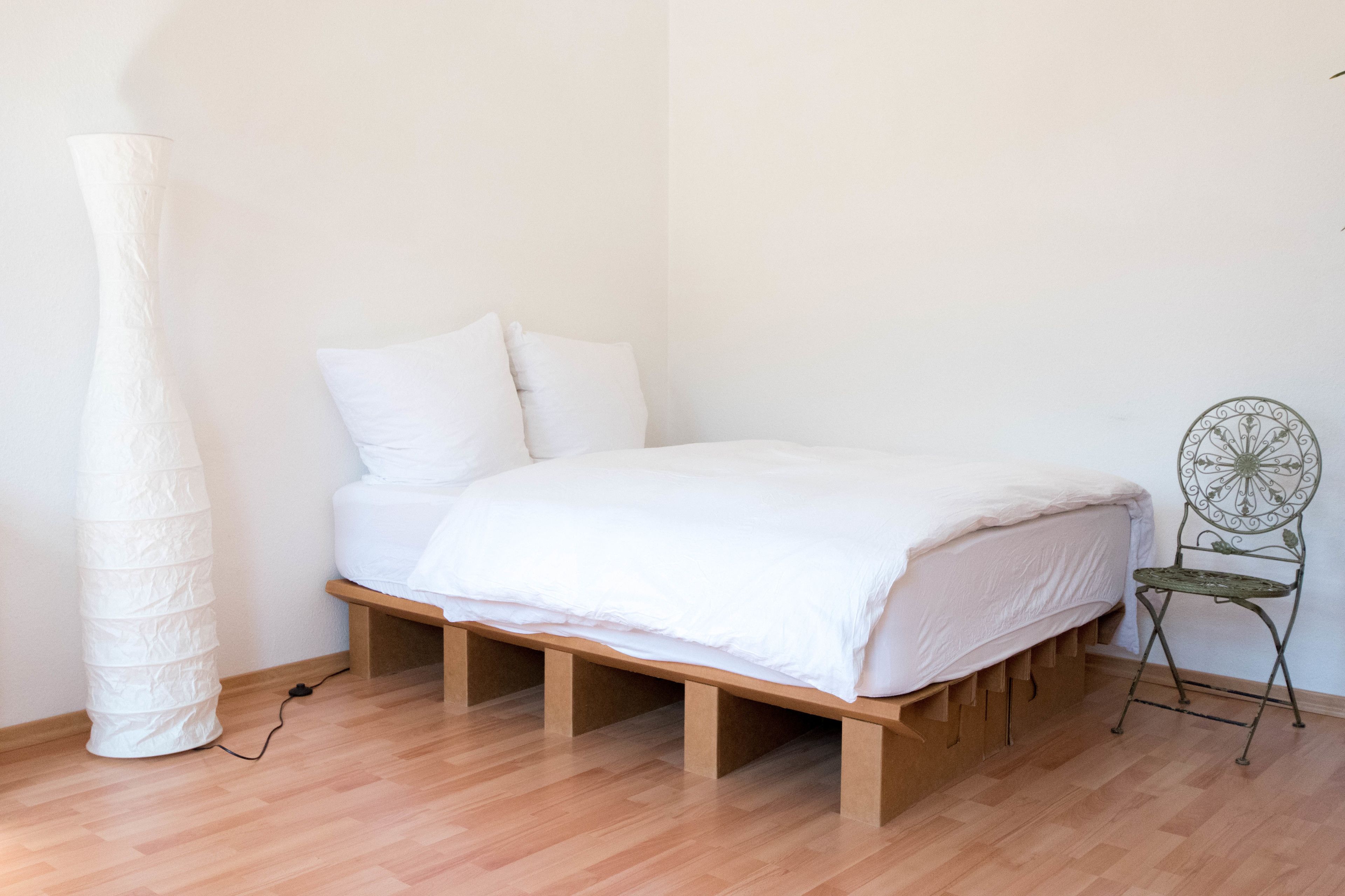 A minimalist bedroom with a wooden bed frame, white bedding, and a tall white vase.