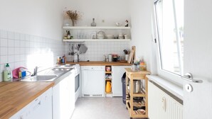 A compact kitchen with white cabinets, a Bosch dishwasher, a wooden countertop, and a window providing natural light. - Peters Wohnung (Weimar)