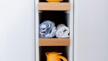 A kitchen area with a white refrigerator, a colorful teapot on a shelf, rolled towels, and a yellow coffee pot.