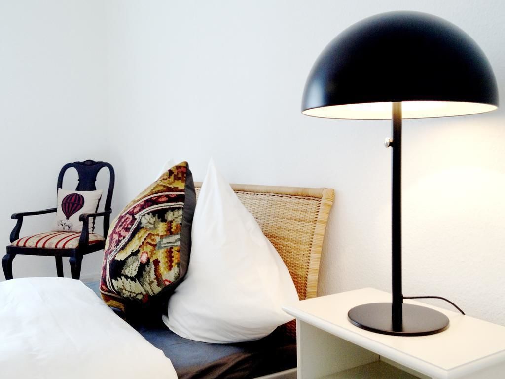 Ein Hotelzimmer mit einem Bett, einem Sessel mit Kissen, einem gemusterten Kopfkissen, einem weißen Kopfkissen und einer schwarzen Stehlampe.