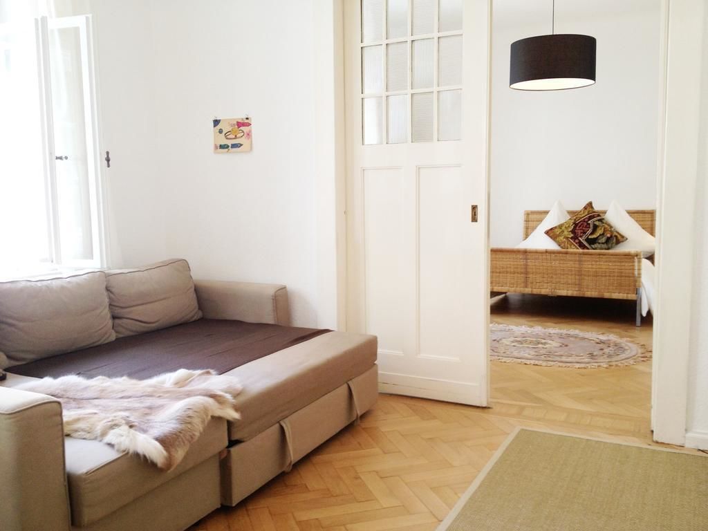 A room with a sofa, a door, a hanging light fixture, and a rug.