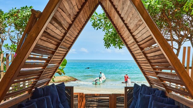 Un espace de détente avec des meubles en bois, offrant une vue sur la plage et l’océan.