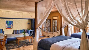 Une pièce avec un lit sous un dais, un hamac, un canapé avec des coussins, une table basse et un tapis à motifs.