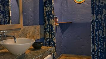 Un baño con un lavamanos blanco, un inodoro y una zona de ducha con cortinas azules estampadas.