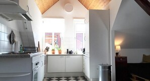 A compact kitchen with white cabinets, a black and white checkered floor, a window with a view of a brick building, and a small trash bin. - Komfort & Stil über Weimars Dächern (Weimar)