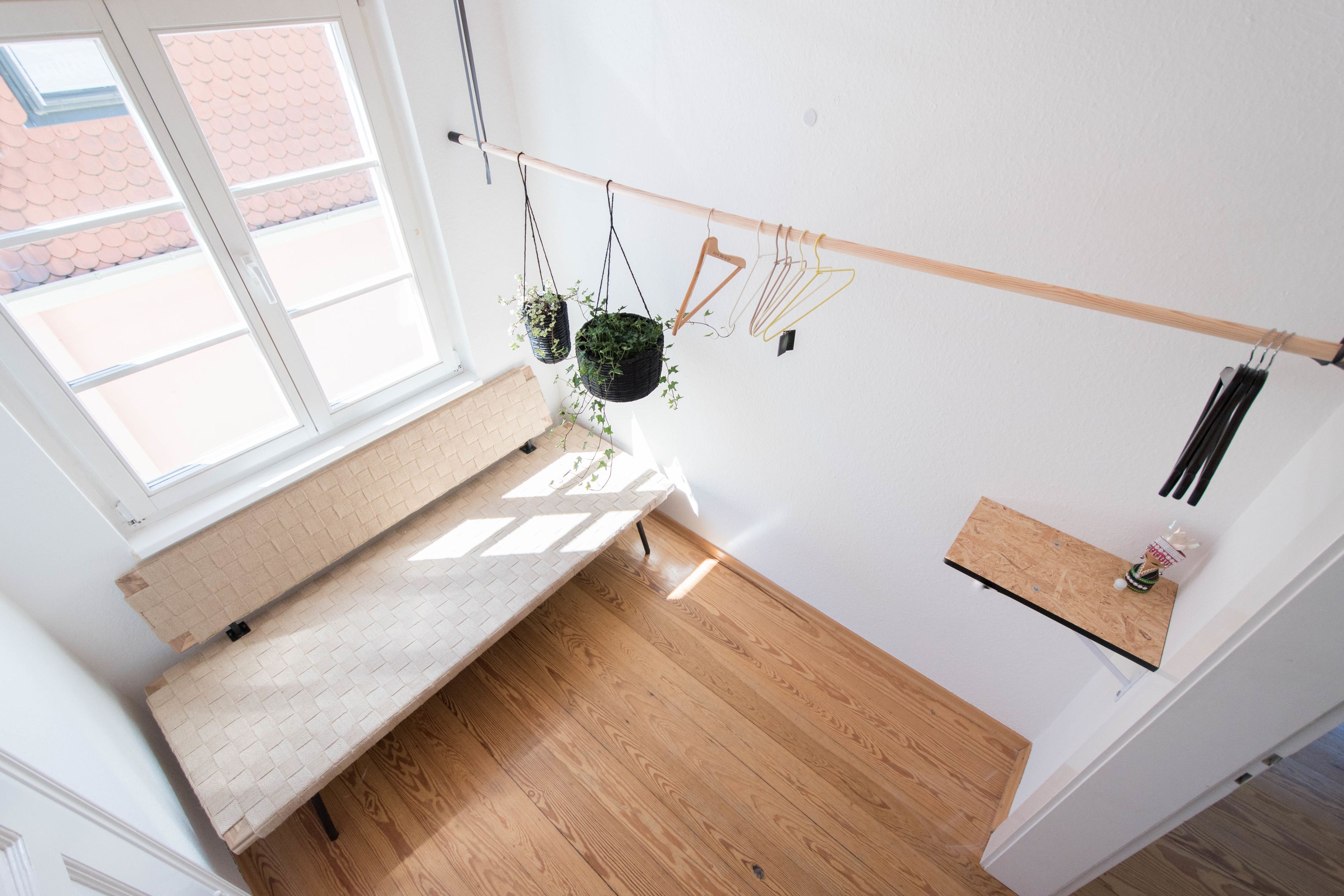 A room with a wooden bench, a window, and a wall-mounted rack with hanging plants and hangers.