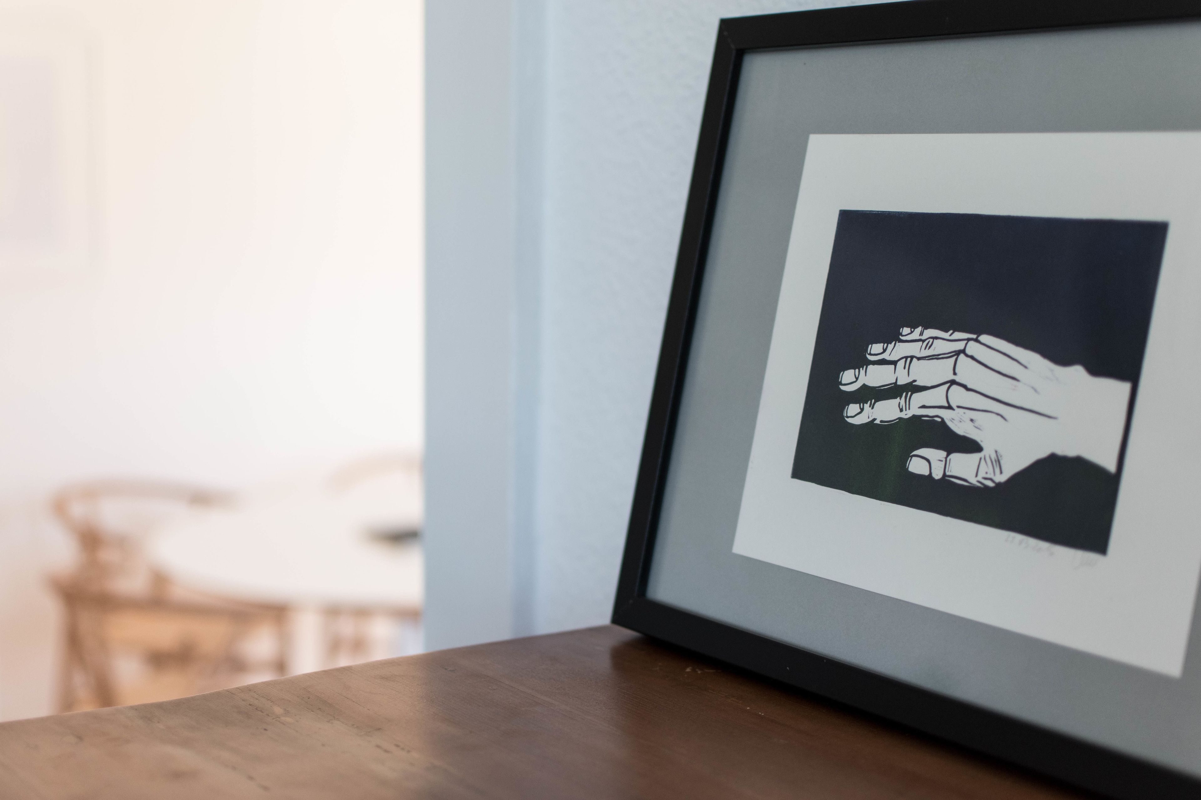 Ein gerahmtes Kunstwerk, das eine Hand auf einer Holzoberfläche zeigt.