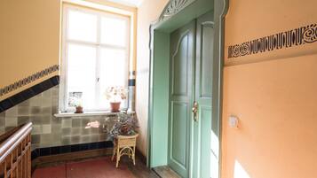 Ein Korridor mit Fliesenboden, einer Holzhandläufe, einem Fenster mit Blumentopf und einer grünen Tür.