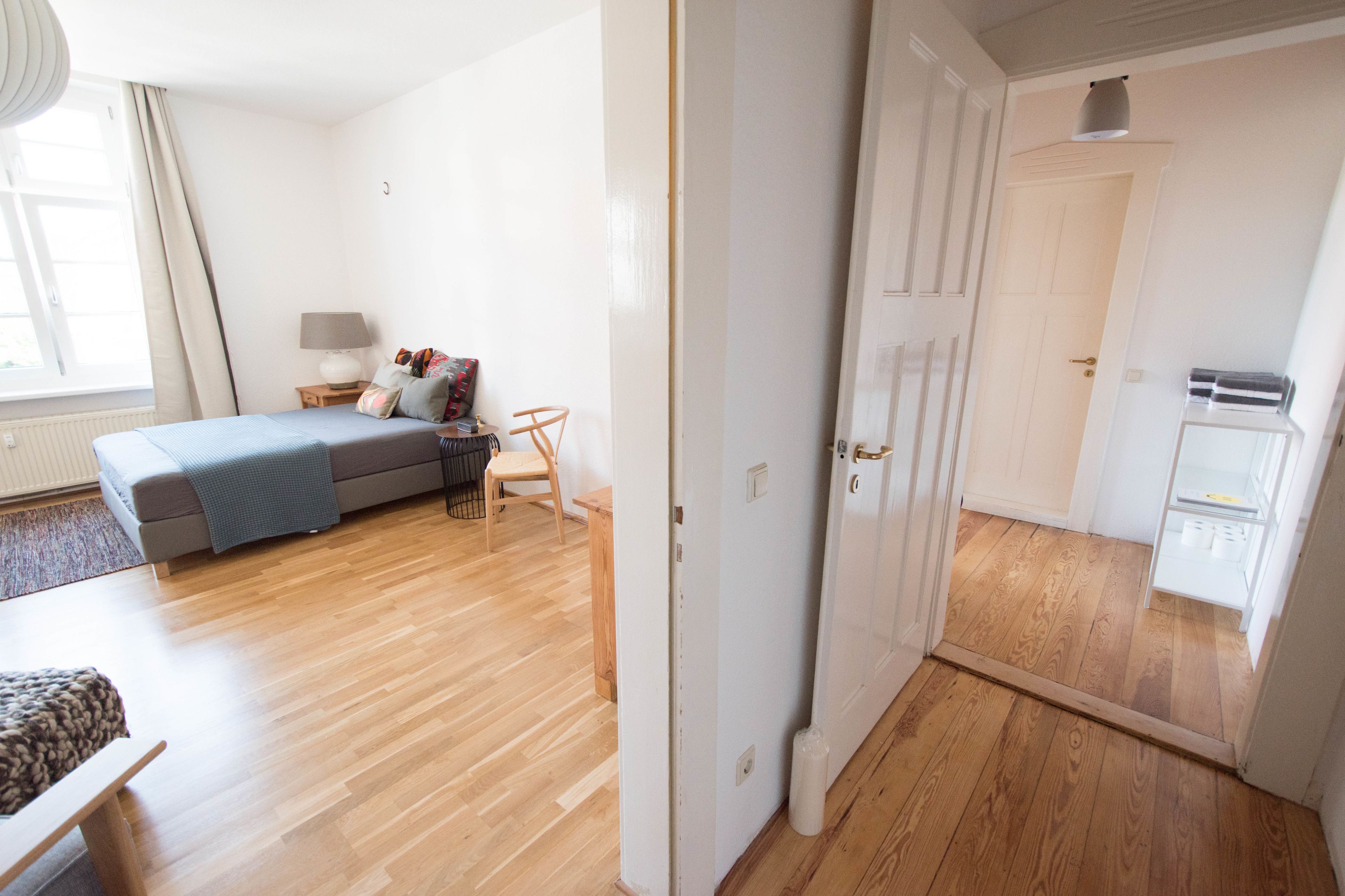 Une chambre moderne avec un lit, une table de chevet, une lampe et une vue sur un couloir menant à une cuisine.