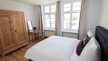 Een slaapkamer met een groot bed, een houten garderobe, een bureau met stoel, en een raam met gordijnen.