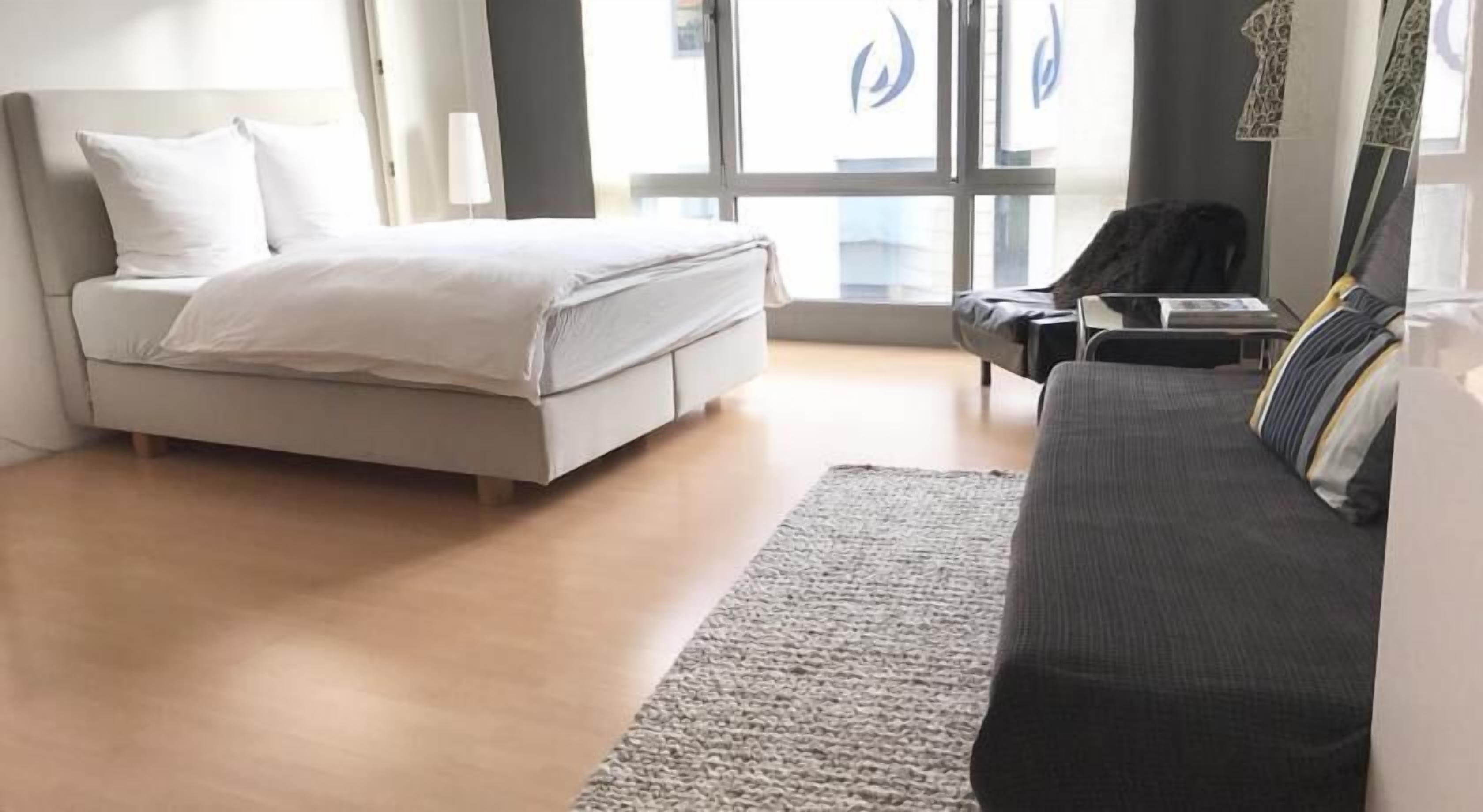 Ein modernes Hotelzimmer mit Bett, Sofa, Schreibtisch und einem großen Fenster.