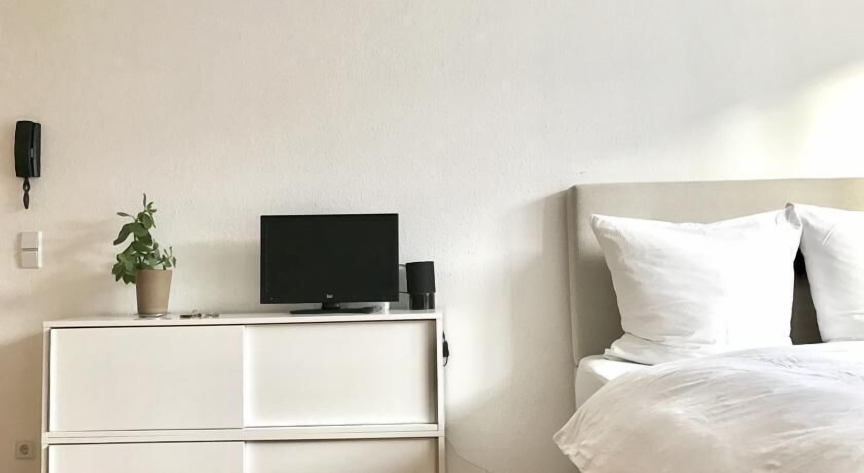 Une chambre d’hôtel avec un lit, une commode blanche, un téléviseur et une plante en pot.