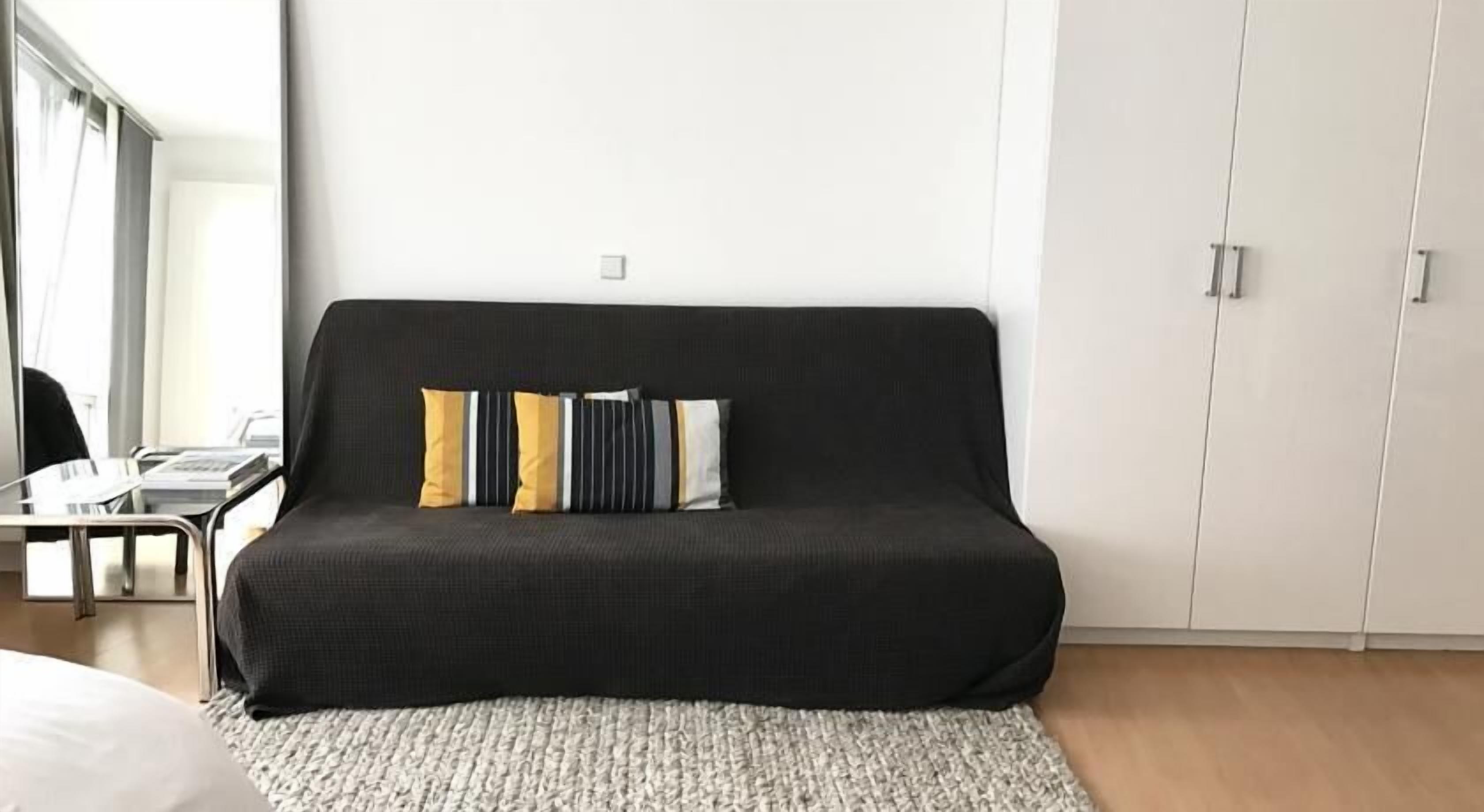A modern room with a black sofa, a white rug, and a wooden floor.