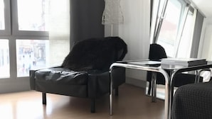 A modern room with a black leather chair, a small table, and a view of the city through large windows. - Central Studio Marktplatz (Weimar)