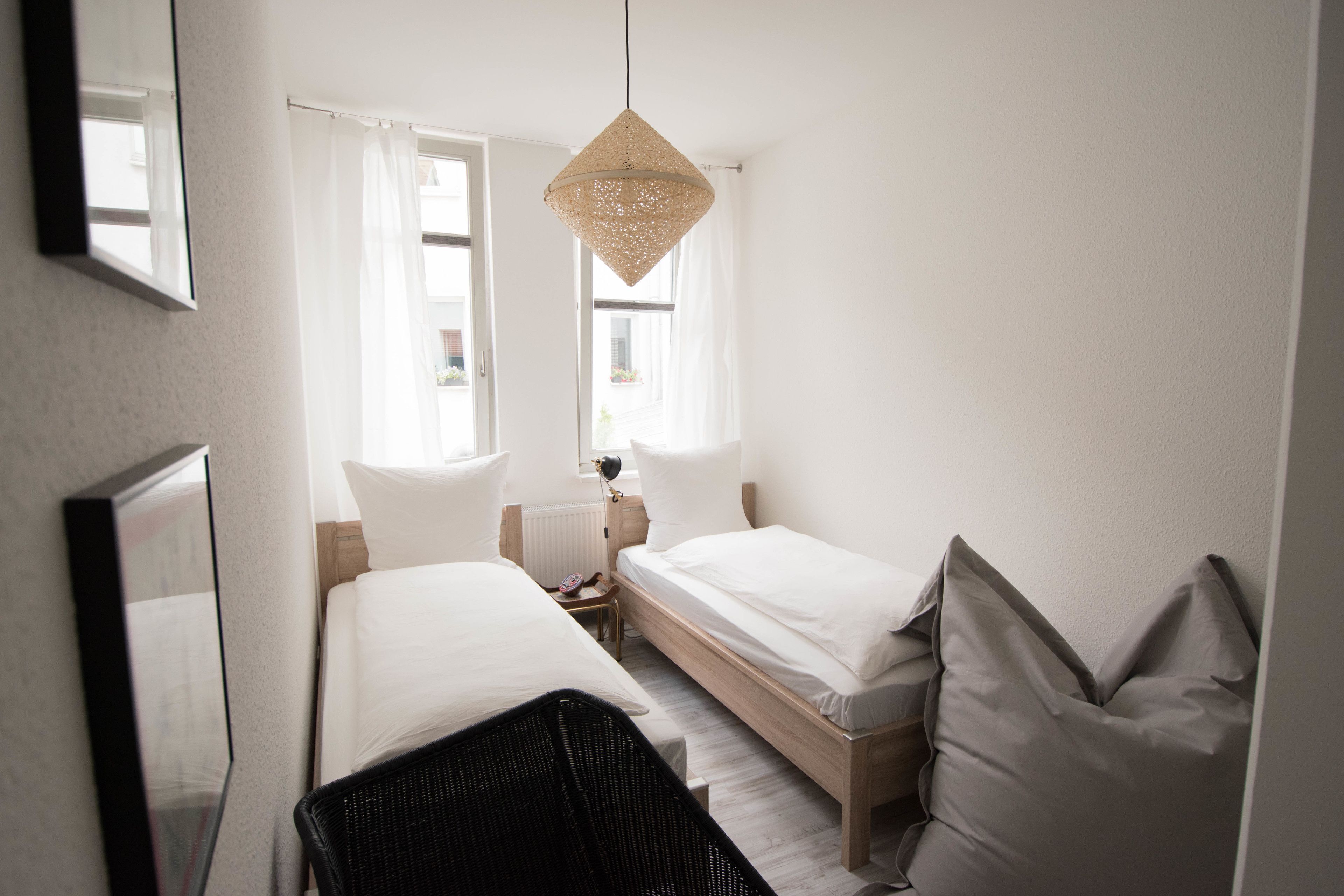 A hotel room with two beds, a large mirror, a hanging light fixture, and a window with curtains.