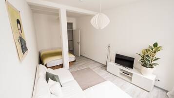 Un dormitorio moderno con cama, sofá, televisor y planta en maceta.