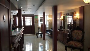 A hotel lobby with a reception desk, a sofa, a chair, and a large mirror. - Hostal Mitad del Mundo (Quito)